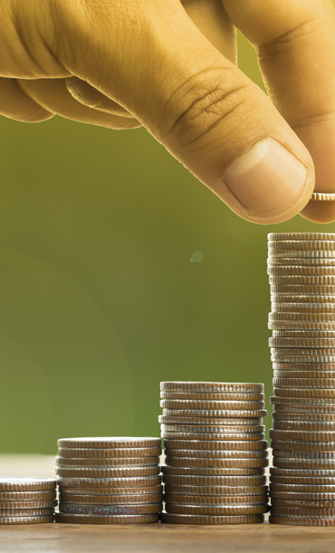 Coins stacked in five piles with a person's hand poised to place another coin on the biggest stack.