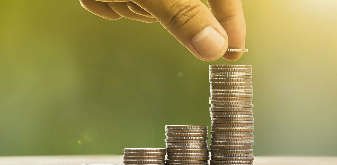 nojs Coins stacked in five piles with a person's hand poised to place another coin on the biggest stack.