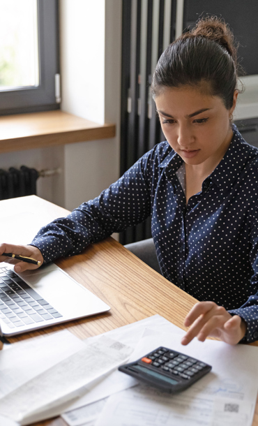 A woman sat working at a desk using a computer and calculator.