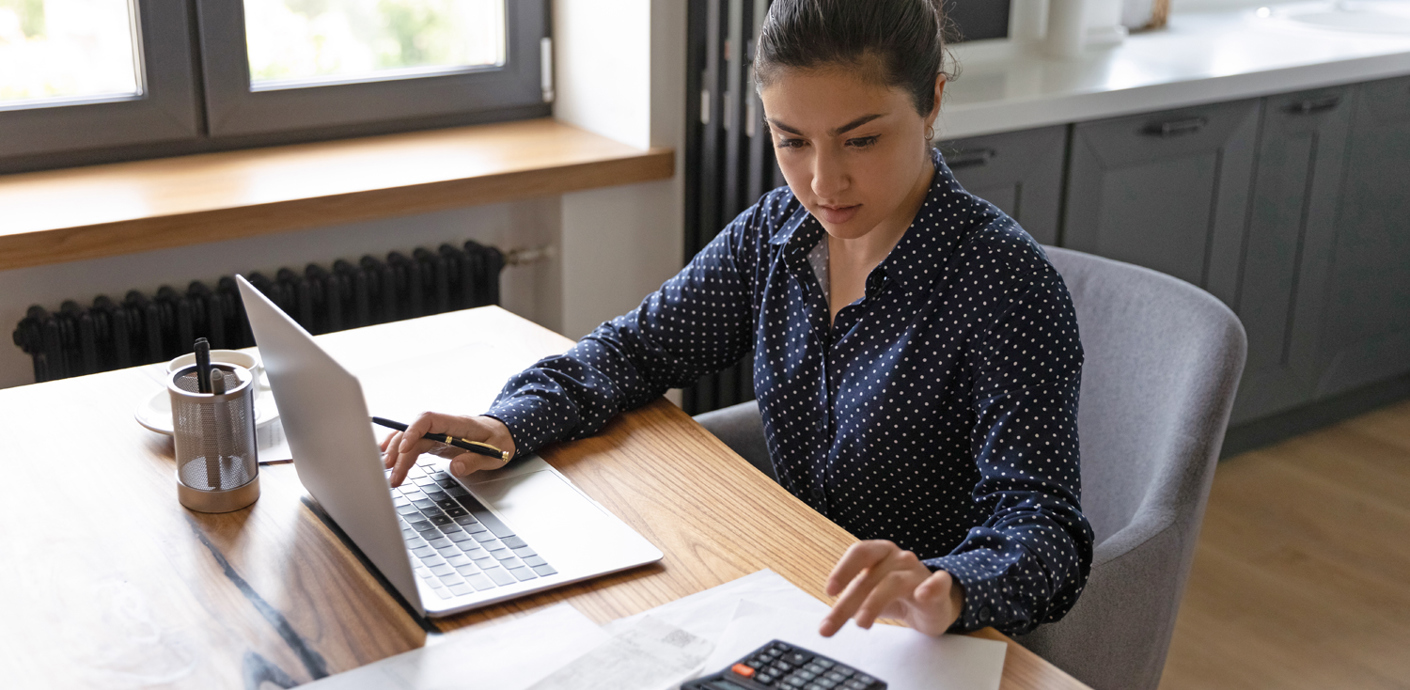 nojs A woman sat working at a desk using a computer and calculator.