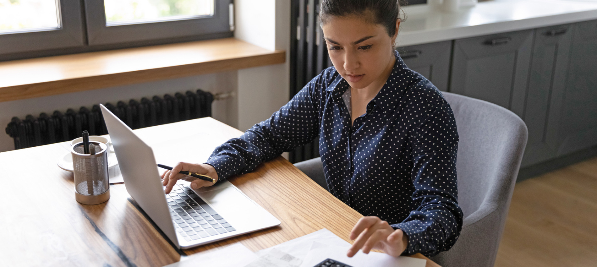 nojs A woman sat working at a desk using a computer and calculator.