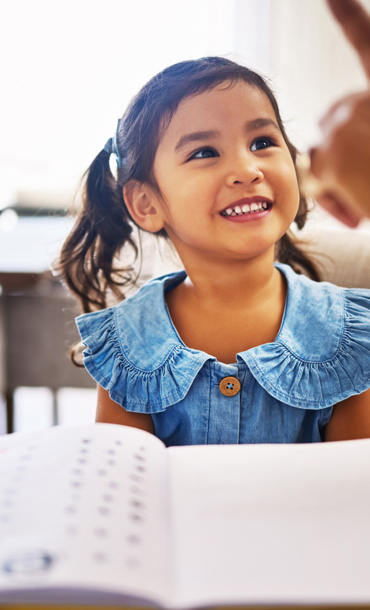 A smiling girl sat at a table being taught maths.