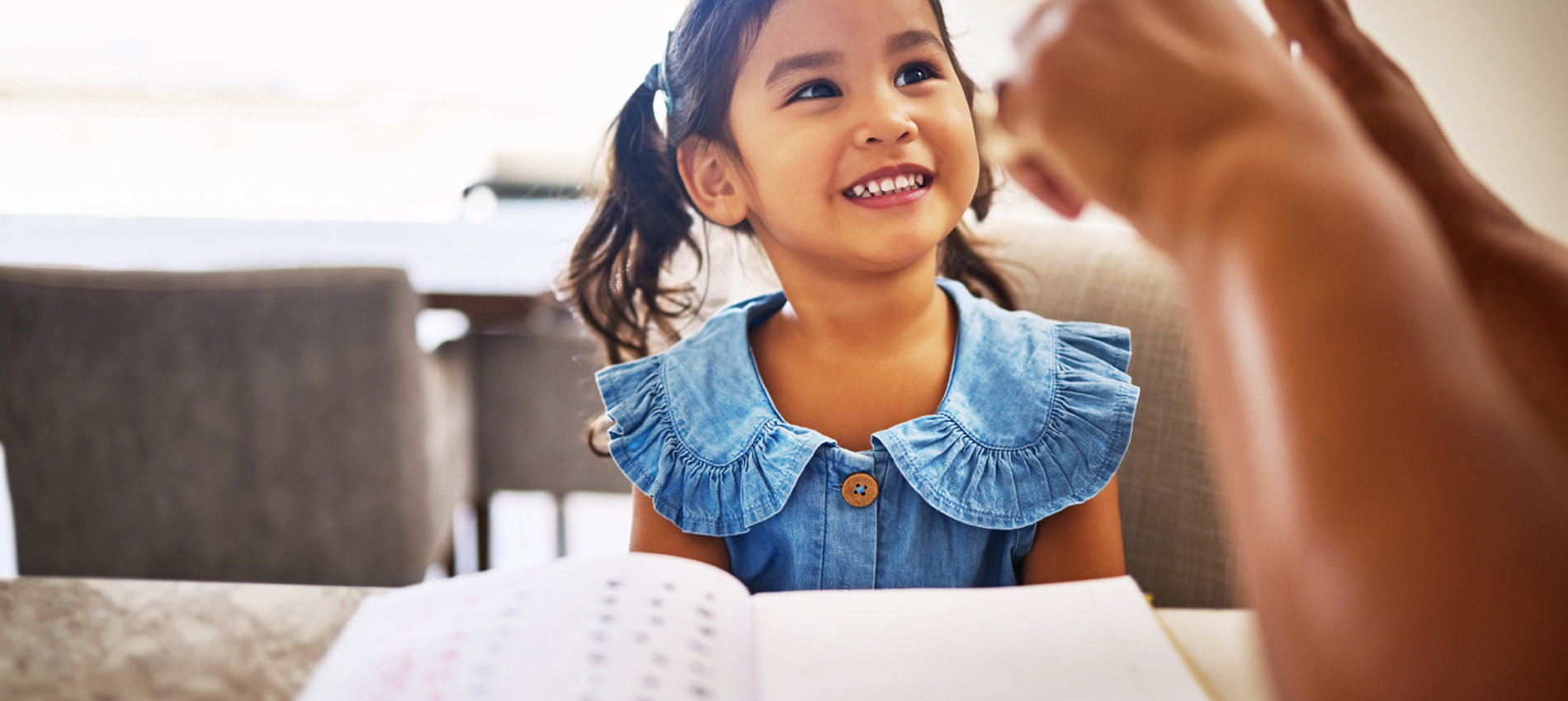 nojs A smiling girl sat at a table being taught maths.