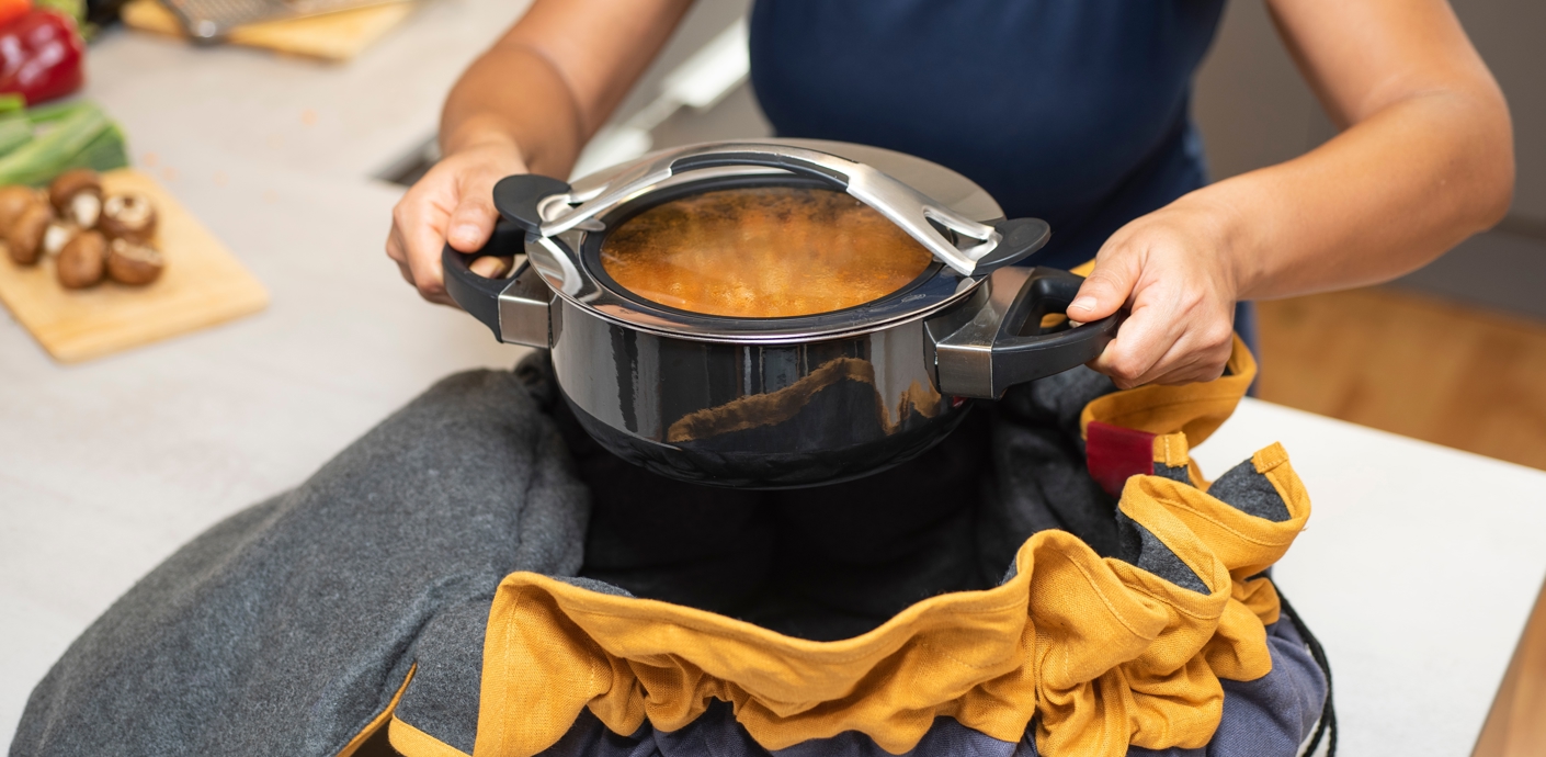 nojs Woman placing cooker into insulating bag to thermally cook a meal.