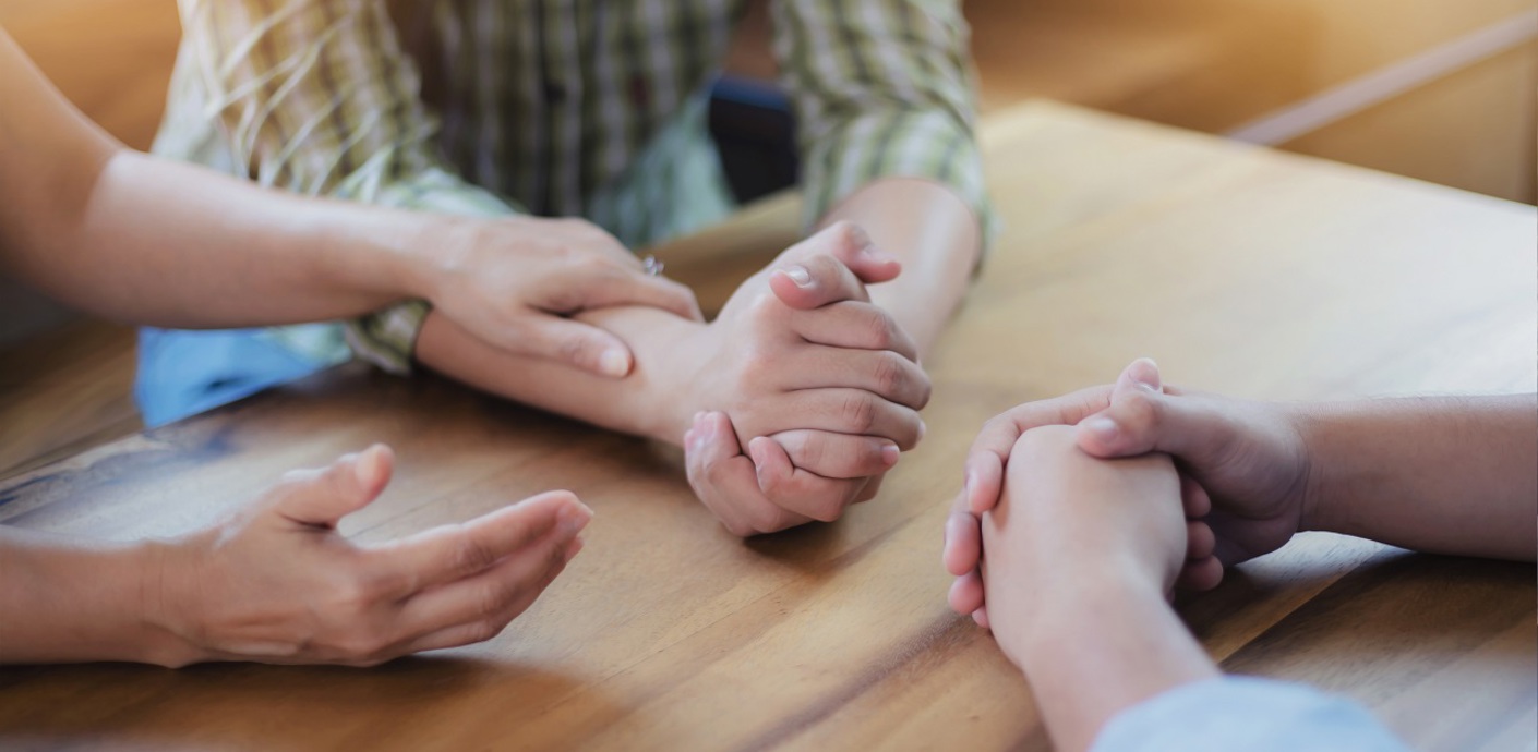 nojs Three people sat round a table in discussion. Only their hands and upper torsos are visible.