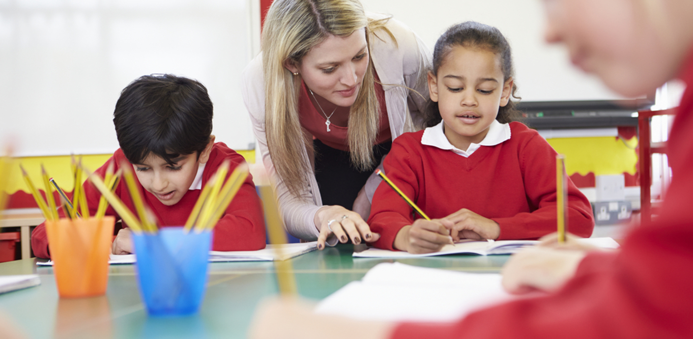 nojs Teacher helping pupils reading and writing.