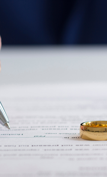 Person signing on paper with two wedding rings
