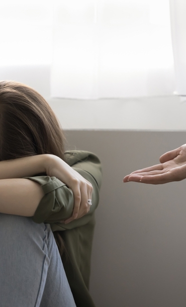 Woman sitting on floor covering head with hands and with another person's outstretched arm offering help